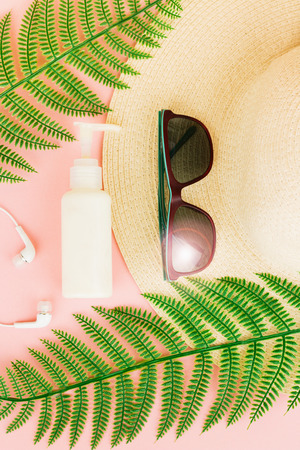 Summer, travel, vacation concept flat lay. Beach accessories: sunscreen lotion, sunglasses, summer hat,  fern and white headphones on pink background. Top view. Space for text.の写真素材