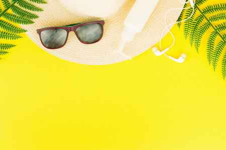 Summer, travel, vacation concept flat lay. Beach accessories: sunscreen lotion, summer hat, sunglasses, fern and white headphones on yellow background. Top view. Space for text.の写真素材