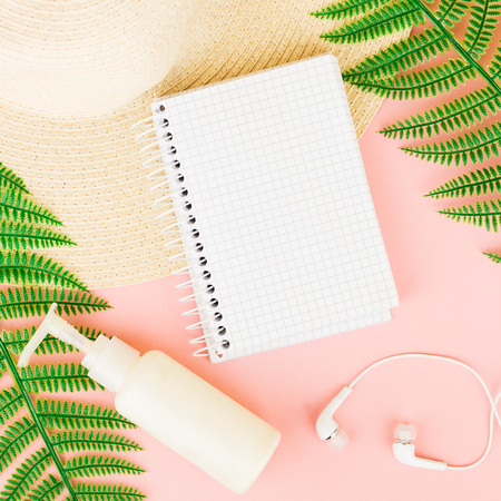 Summer, travel, vacation concept flat lay. Beach accessories: sunscreen lotion, notebook, summer hat,  fern and white headphones on pink background. Top view. Space for text.の写真素材