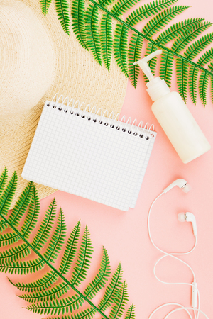 Summer, travel, vacation concept flat lay. Beach accessories: sunscreen lotion, notebook, summer hat,  fern and white headphones on pink background. Top view. Space for text.の写真素材