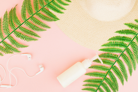 Summer, travel, vacation concept flat lay. Beach accessories: sunscreen lotion, summer hat,  fern and white headphones on pink background. Top view. Space for text.の写真素材