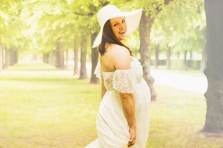 Pregnancy, love, people and expectation concept - happy pregnant woman posing over green natural background in white dress and hat, Copy space for text with toned effect.の写真素材