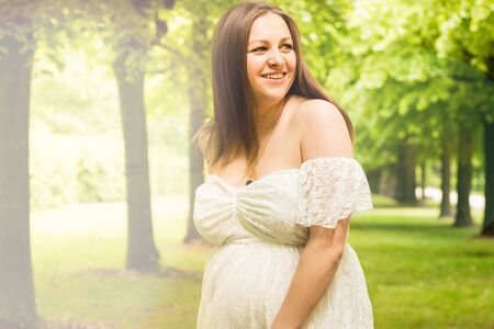 Pregnancy, love, people and expectation concept - happy pregnant woman posing over green natural background in white dress, Copy space for text with toned effect.の写真素材