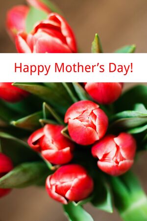 Spring theme. Mother's Day festive background. The bouquet of red tulips on brown background. Close up. Top view with text Happy Mother's Day.の写真素材