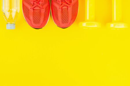 Sport background. Yellow dumbbells, a bottle of fresh water and pink sneakers on yellow background. Still life and health care concept. Flat lay, view from above. Copy space for text.の写真素材