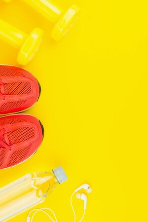 Sport background. White headphones, yellow dumbbells, a bottle of fresh water and pink sneakers on yellow background. Still life and health care concept. Flat lay, view from above. Copy space for text.の写真素材