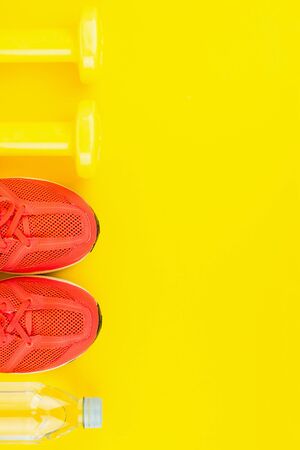 Sport background. Yellow dumbbells, a bottle of fresh water and pink sneakers on yellow background. Still life and health care concept. Flat lay, view from above. Copy space for text.の写真素材
