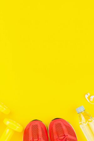 Sport background. White headphones, yellow dumbbells, a bottle of fresh water and pink sneakers on yellow background. Still life and health care concept. Flat lay, view from above. Copy space for text.の写真素材