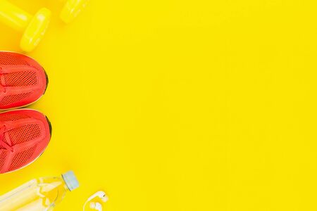 Sport background. White headphones, yellow dumbbells, a bottle of fresh water and pink sneakers on yellow background. Still life and health care concept. Flat lay, view from above. Copy space for text.の写真素材