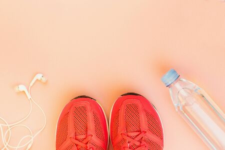 Sport background. White headphones, a bottle of fresh water and pink sneakers on pink background....