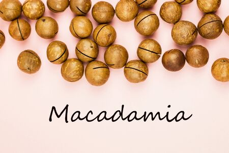Raw not peeled whole macadamia nuts on pink background. Healthy food. Protein source. Flat lay. View from above with text Macadamia.の写真素材