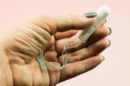 Close up of woman hand holding menstruation cotton tampon on pink background with copy space for text. Feminine hygiene product,の写真素材