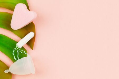 Close up of menstrual cup, tampon and sponge on pink background and green tropical leaf with copy space for text. Feminine hygiene products, View from above.の写真素材