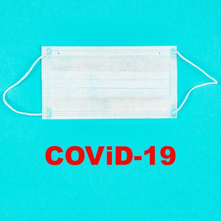 A close up of medical mask on blue background with text covid-19. Coronavirus protection. Copy paste for text. Top view. Flat lay.の写真素材