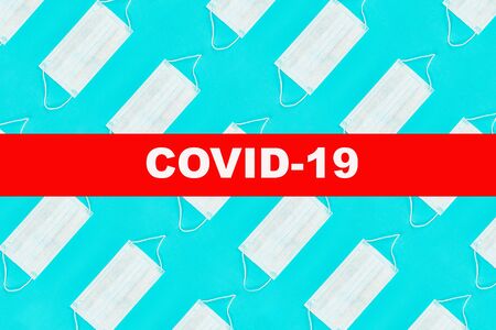 Pattern of face medical masks on blue background with text covid-19. Protection from coronavirus. Top view. Flat lay.の写真素材
