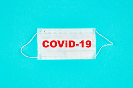 A close up of medical mask on blue background with text covid-19. Coronavirus protection. Copy paste for text. Top view. Flat lay.の写真素材