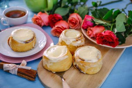 bun with cinnamon and kremoi on a pink plate in a romantic setting with rosesの写真素材
