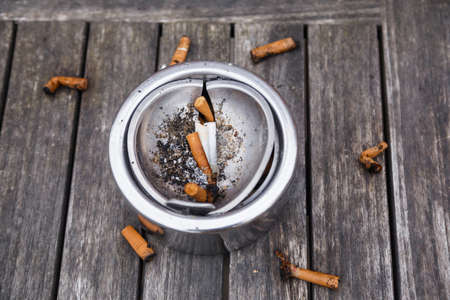 Cigarette butts with ash in ashtray on grey wooden table.の写真素材