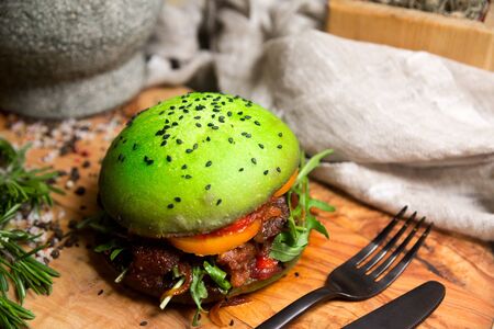 Homemade burger made of green dough. Green bun, with caramelized onions, a slice of orange tomato, with arugula leaves, barbecue sauce, grilled meat.の写真素材