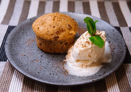 Carrot cake with a melted ball of cream ice cream decorated with mint leaves on a gray ceramic plateの写真素材