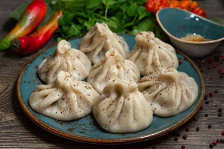 Georgian-style khinkali with meat on a handmade ceramic plate. Sprinkled with ground pepper. Leaves of parsley and coriander in the background. On a dark gray wooden kitchen table.の写真素材