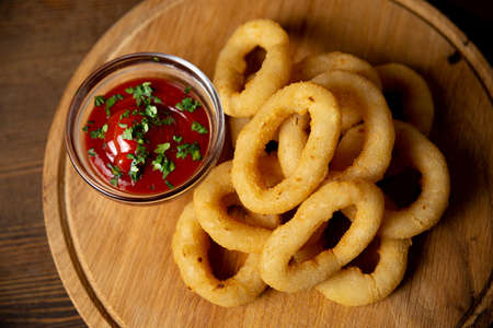 Onion rings with ketchup on a wooden board. Bar food. One serving. Sprinkled with ground pepper.の写真素材