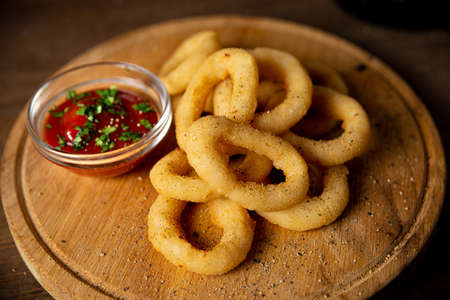Onion rings with ketchup on a wooden board. Bar food. One serving. Sprinkled with ground pepper.の写真素材