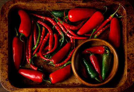 A scattering bunch of red chilies and green Romano peppers on a wooden tray. Colorful juicy hot peppers. Shot from above.の写真素材