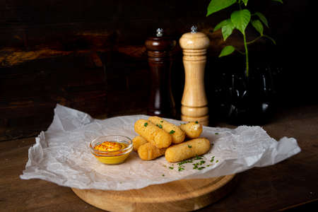 A portion of cheese sticks, served on a wooden board with mustard. Bar deep fried food. Shot in the interior of a bar against a dark wooden background.の写真素材