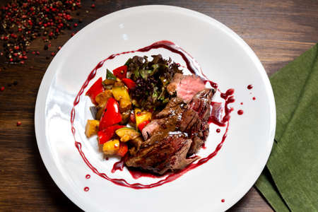 Chateaubriand of tender beef in Bordeaux wine sauce with vegetable sautÃ©. Large plate of food on a dark brown wooden backdrop.の写真素材
