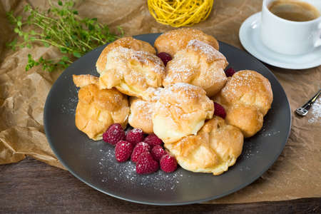 A pile of profiteroles sprinkled with powdered sugar. Served with fresh raspberries and coffee.の写真素材