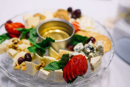 Glass plate with appetizers on the banquet table. Cheeses, walnuts, honey, grapes, mint leavesの写真素材