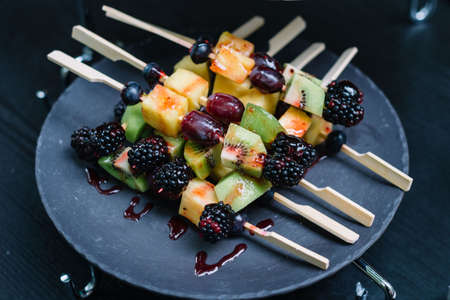 Appetizers on plates. catering service. Fruits on skewers (blueberries, blackberries, kiwi, pineapple). Welcome buffet at the event.の写真素材