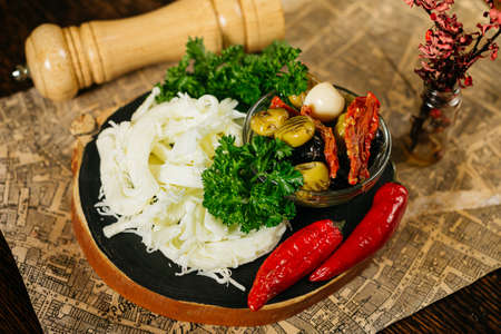 Bar snacks portion on wooden board: cecil cheese, hot peppers, olives, sun-dried tomatoes, fresh parsley leaves.の写真素材
