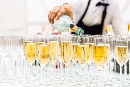 The bartender is pouring champagne into glasses. Glasses of champagne on the bar. Lots of alcoholic drinks.の写真素材