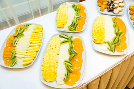 Sliced tropical fruit slices on plates. Hotel catering, buffet table. Sliced pineapple, kiwi, orange and melon.の写真素材