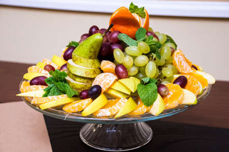 fruit plate. Stylishly lined fruit: orange slices, pear slices, grapes, tangerine, mint leaves. Catering serving on a glass base.の写真素材