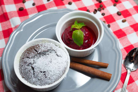 A portion of chocolate fondant in a ramekin sprinkled with powdered sugar next to a portion of berry sorbet garnished with mint leavesの写真素材