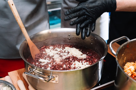 The red beans are cooked (boiling with garlic) in a saucepan on the stove. a black-gloved hand stirs...