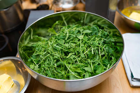 A deep metal bowl of washed arugula leaves, view slightly above, ready to cook