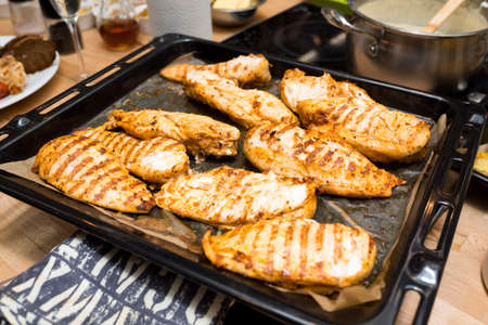Grilled chicken breast meat. Lots of portions on a baking tray.
