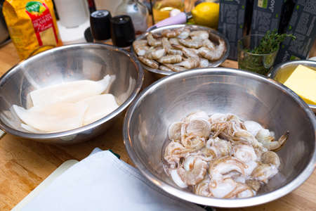 Raw seafood in a metal bowl. cooking preparations. Bowl with uncooked shrimp. Bowl with raw squid. Table with billets.の写真素材