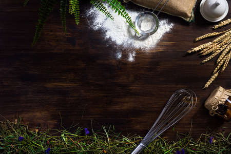 Utensils flat lay whisk, flour, a bag, a sieve, a jar of jam, straw, hay, oatmeal ears, sprinkled...