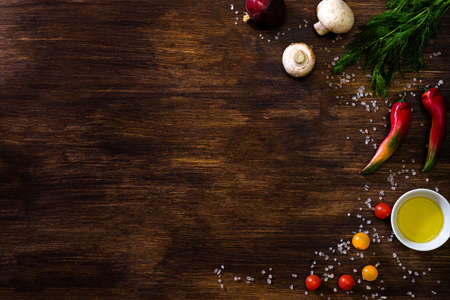 Wooden dark background culinary theme copy space with champignon mushrooms, chilli peppers, hot peppers, salt, oil, vegetable oil, dill, greens, herbs, onions, cherry tomatoes, tomatoes.の写真素材