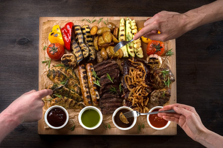 A board with grilled appetizers and sauces. Grilled vegetables and meat snacks: sausages, chicken fillets, pork and beef steaks.の写真素材