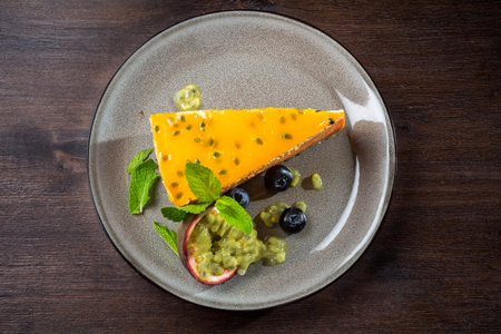 Passion fruit cheesecake. A delicate dessert portion with fresh passionfruit wedges and blueberries on a plate. The dessert is sprinkled with powdered sugar.の写真素材