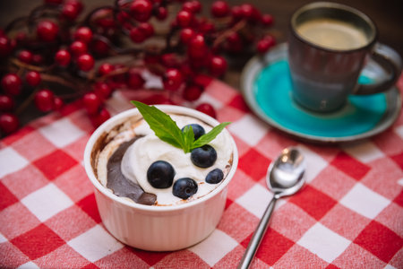 Dessert parfait with chocolate sauce, blueberries, garnished with fresh mint leaves. Serve the dessert with a cup of coffee on a red checkered cloth napkin.の写真素材