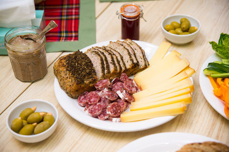 Plate with appetizers, sliced cheese, sausages, olives and nuts, bread with spices and cereal, jar...