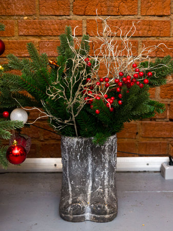 Artificial pine branches with red berries in cement boots. An element of interior decor. brick wall in the background.の写真素材