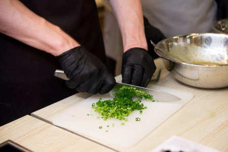 Chef's hands in black gloves chopping greens on board, cooking processの写真素材